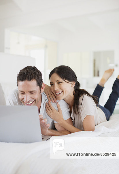 Couple using laptop on bed