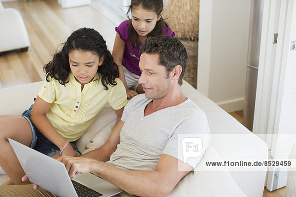 Vater und Töchter mit Laptop auf Sofa im Wohnzimmer