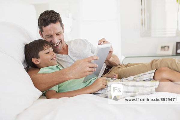 Vater und Sohn mit digitalem Tablett auf dem Bett