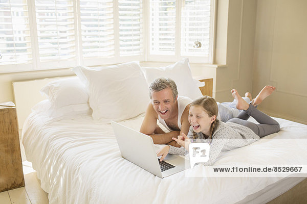 Vater und Tochter mit Laptop im Bett