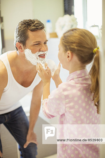 Mädchen reibt Rasiercreme auf Vaters Gesicht