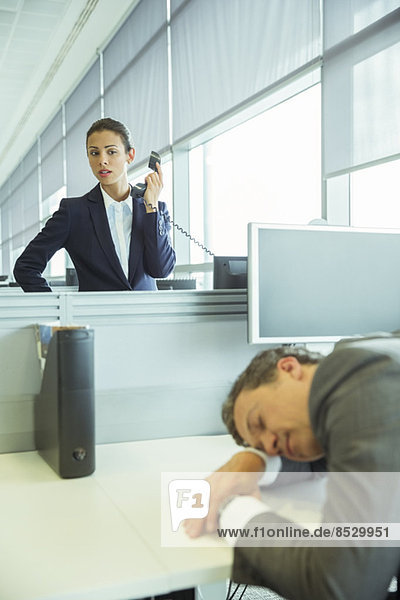 Geschäftsfrau beobachtet schlafenden Geschäftsmann im Büro