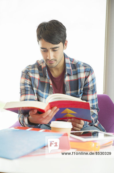 Universitätsstudent liest Lehrbuch in der Lounge