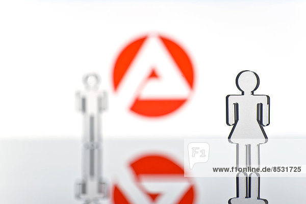 Zwei Figuren vor dem Logo der Arbeitsagentur  Symbolbild für Arbeitslosigkeit