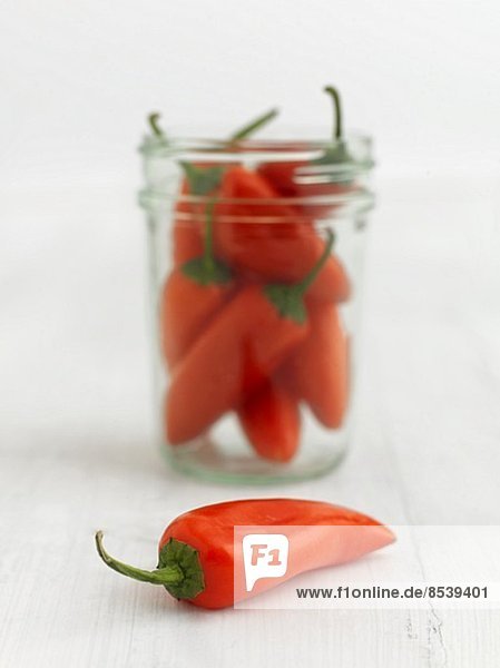 Whole orange chillies in front of and in a jar