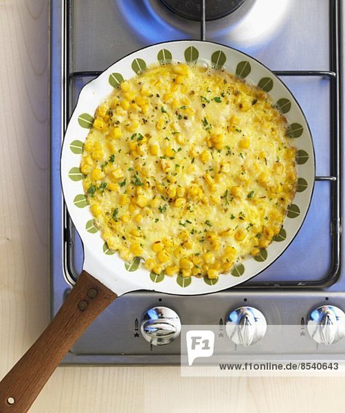 Sweetcorn omelette in a frying pan on a gas hob (view from above)