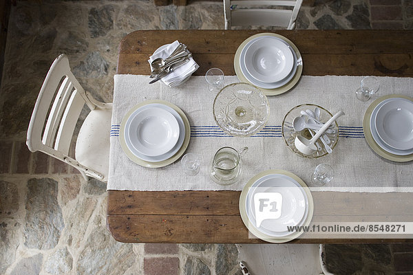 Eine Draufsicht auf einen mit weißem Geschirr und Glaswaren gedeckten Tisch.