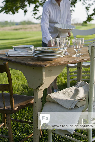 Ein in einem Garten gedeckter Tisch mit weißem Porzellangeschirr und Besteck. Sommer.