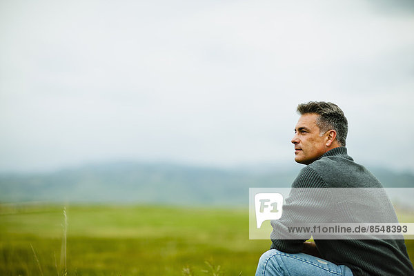 Ein Mann,  der allein sitzt und in die Ferne schaut,  tief in Gedanken versunken.