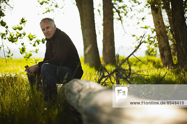 A man sitting on a fallen tree trunk in woodland.