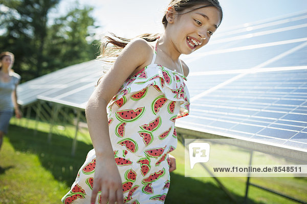 A child and her mother in the fresh open air  beside solar panels on a sunny day at a farm in New York State  USA.