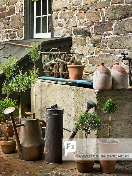 A collection of old watering cans  and clay pots for plants  outside a house.