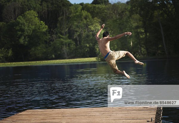 Ein Junge  der mit Anlauf von einem Holzsteg in ein ruhiges Wasserbecken springt.