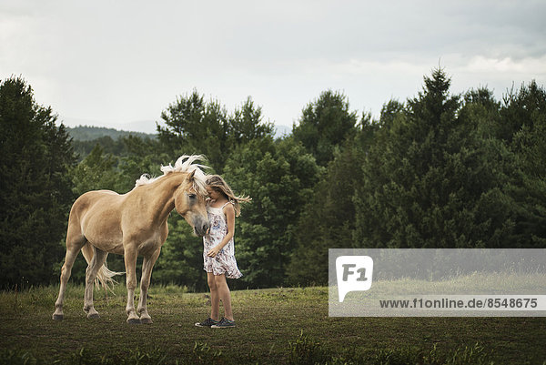 Ein junges Mädchen mit einem Palomino-Pony auf einem Feld.