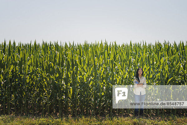 A young woman standing with arms folded  in front of a very tall maize  corn crop in the field.