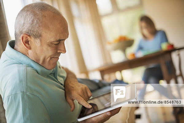 Ein Mann sitzt in einer traditionellen Bauernküche und benutzt einen elektronischen Tablet-Computer.