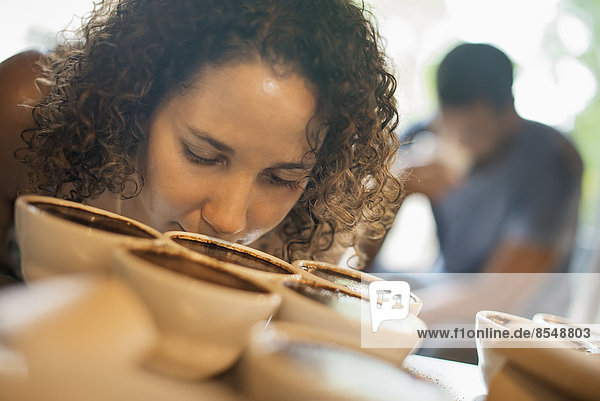 Eine Frau probiert in einer Kaffeeverarbeitungshalle  in der das Personal Kaffee in kleinen Kannen zubereitet und den Geschmack probiert  um die Mischung zu testen.