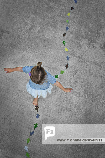 View from overhead of a child creating and walking along a line of coloured leaf shapes.