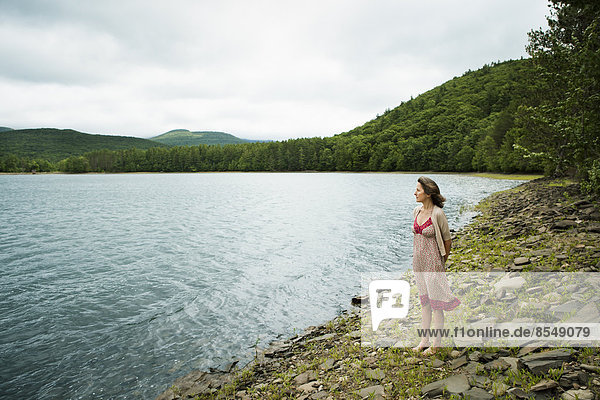 A woman in open countryside  by a mountain lake.