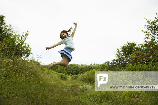 Ein junges Mädchen,  das vor Freude hüpft und die Fersen in die Luft streckt.