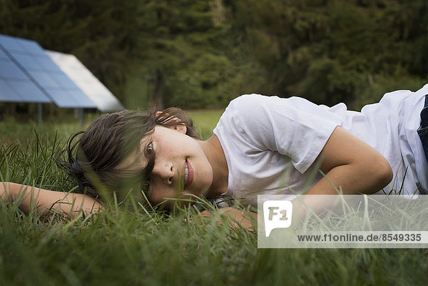 A boy lying in the grass  beside a solar panel.