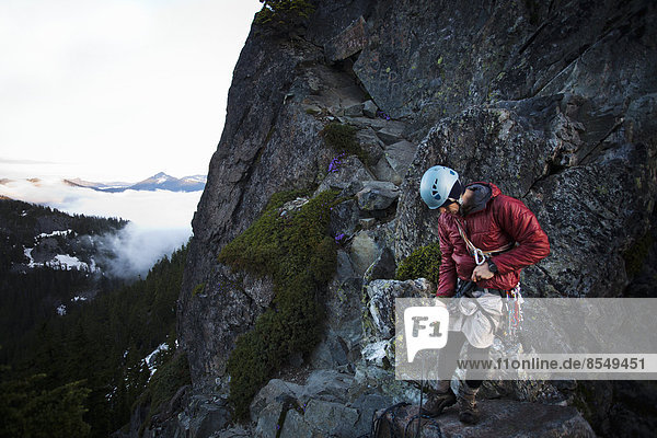 Ein Felskletterer steht auf dem Gipfel eines Gipfels  nachdem er mit Hilfe eines Seils auf den Gipfel geklettert ist.