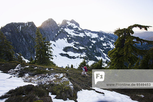 A young man hikes around a snow patch while going to the summit of a large mountain in the Cascades of Washington  USA.