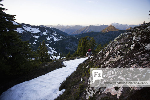 Ein junger Mann klettert um eine Schneefläche herum  während er auf den Gipfel eines großen Berges in den Cascades of Washington  USA  wandert.