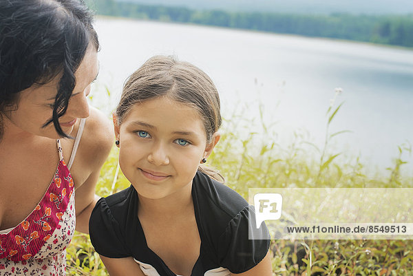A mother and daughter in long grass by a lake shore.