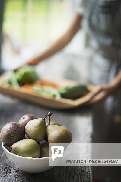 Eine Person,  die in einer Küche Bio-Gemüse zubereitet. Tablett mit Gemüse. Schale mit Birnen.