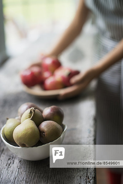 Eine Person  die in einer Küche frische Bio-Produkte zubereitet. Tablett mit roten Äpfeln. Schale mit Birnen.