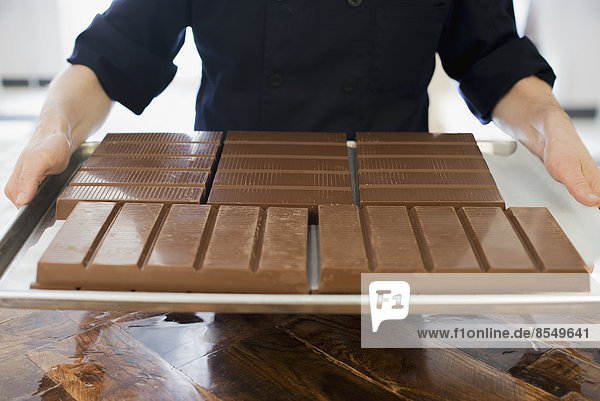 Herstellung von Bio-Schokolade. Eine Person  die ein Tablett mit Tafeln aus verarbeiteter Schokolade hält.