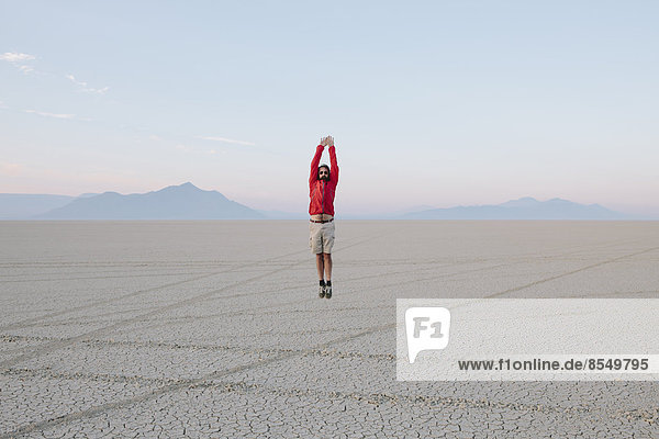 Ein Mann  der in der flachen Wüste oder Playa oder Black Rock Desert  Nevada  in die Luft springt.