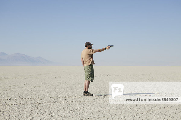 Man aiming hand gun  standing in vast  barren desert