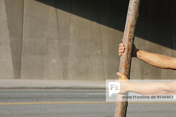 Man pulling on a small tree  on a city sidewalk.