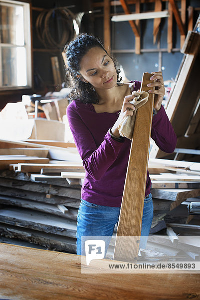 Eine Frau  die in einer Holzwerkstatt mit wiedergewonnenem Holz arbeitet.