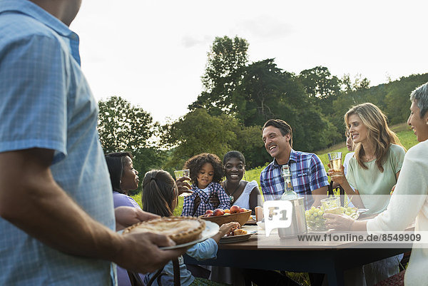 Eine Familie und Freunde  die an einem Tisch im Freien sitzen und eine Mahlzeit einnehmen.
