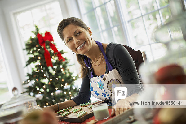 Eine Frau  die an selbstgebackenen Bio-Weihnachtsplätzchen arbeitet und Dekorationen auf grünem Zuckerguss dekoriert und bestreut.