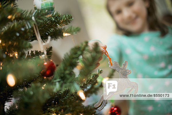 A young girl placing a homemade Christmas ornament on a tree.