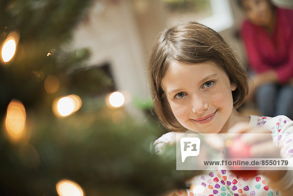A girl placing a handmade ornament on a Christmas tree.
