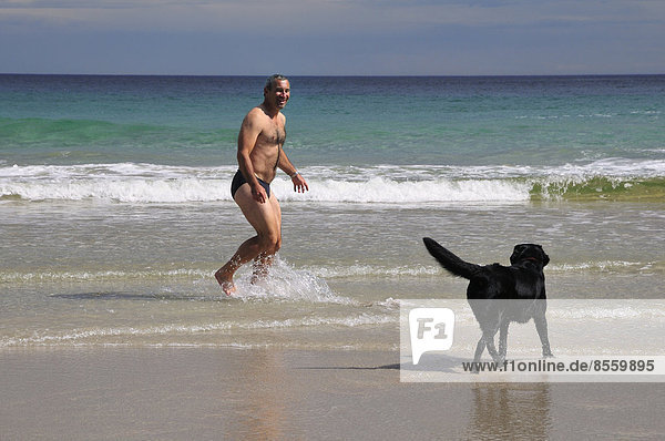 Man in swimming trunks playing with a dog on the beach of Rispond Bay  Durness  Caitness  Sutherland and Easter Ross  Scotland  United Kingdom