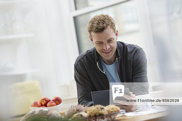 An office or apartment interior in New York City. A man in a sweatshirt top using a digital pad. Leaning on a breakfast bar.