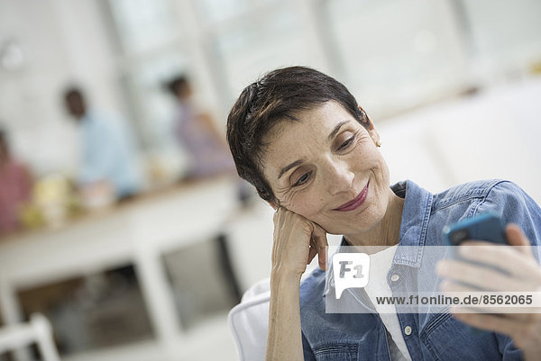 Ein Großraumbüro in New York City. Eine reife Frau mit grauen Haaren  die ein Jeanshemd trägt und auf den Bildschirm eines Smartphones schaut.