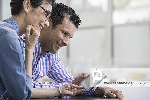 Fachleute im Büro. Ein heller und luftiger Arbeitsplatz. Zwei Personen sitzen an einem Schreibtisch und benutzen ein digitales Tablett. Arbeitskollegen.