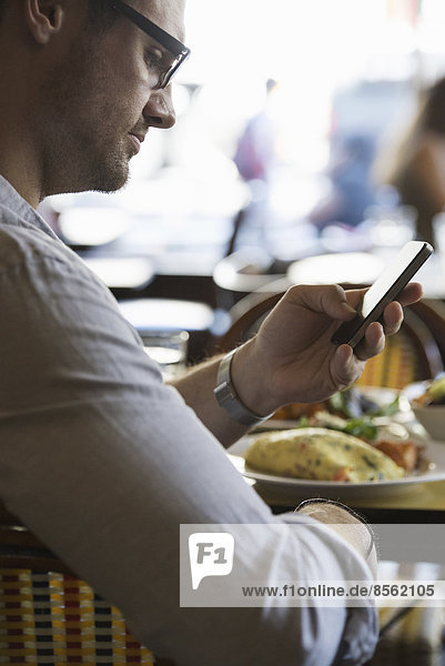 Unterwegs in Kontakt bleiben. Ein Mann in legerer Kleidung sitzt an einem Cafétisch und überprüft sein Smartphone.