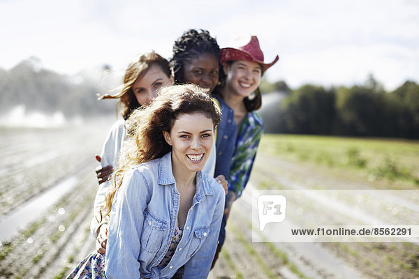 Vier junge Frauen auf einem Feld voller Setzlinge  einer Bio-Kulturpflanze  mit Sprinklern  die im Hintergrund Wasser versprühen.