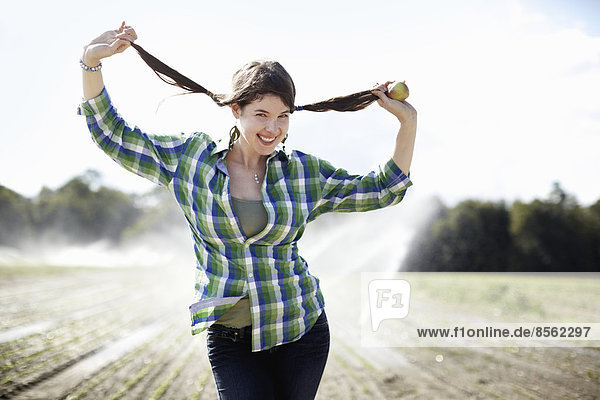 Ein Mädchen in einem grün karierten Hemd mit Zöpfen steht in einem Feld mit Sprinklern  die im Hintergrund arbeiten.