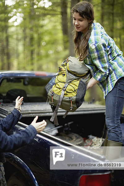 Eine junge Frau entlädt Rucksäcke von der Ladefläche eines Pick-ups.