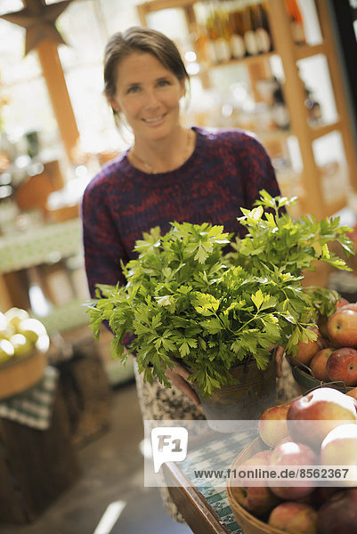Biolandwirt bei der Arbeit. Eine Frau arbeitet an einem Bauernstand mit einer Ausstellung von frischen Produkten. Grüne Pflanzen und Schalen mit Äpfeln.