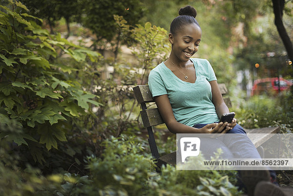 Szenen aus dem städtischen Leben in New York City. Ein junges Teenager-Mädchen sitzt auf einer Bank  schaut auf einen Bildschirm oder schreibt eine SMS.